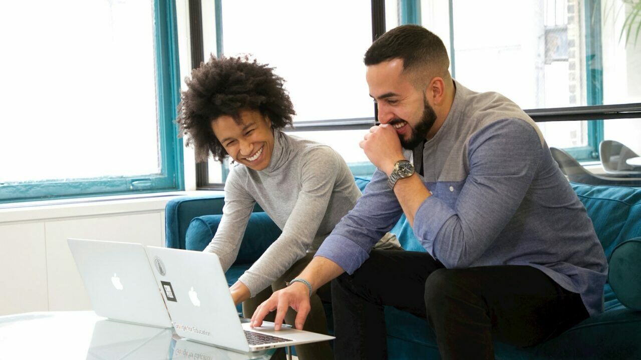 a man and woman sitting on a couch looking at a laptop